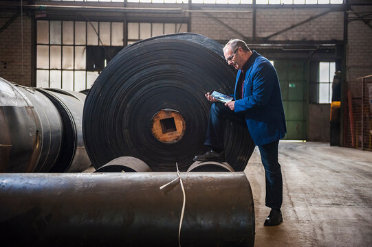 Businessman using tablet in warehouse with large rubber rollers