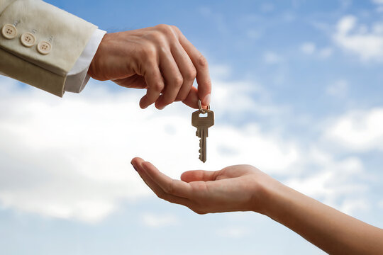 Hand passing metal key to open palm against blue sky exchange receiving