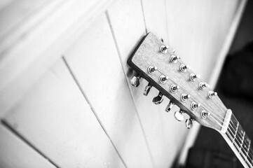 The head and neck of an acoustic 12 string guitar leaning against a wall in monochrome - vertical