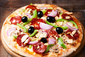 Pizza with chorizo ​​sausage, mozzarella cheese, green pepper and black olives. Rustic wooden background. Soft focus.	