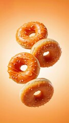 Four glazed donuts with sprinkles suspended in mid-air against a warm orange background