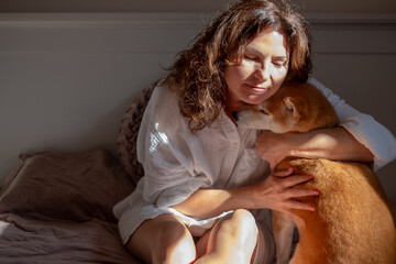 Shiba Inu dog snuggles with woman in cozy morning light, showcasing warmth and companionship in a...