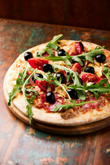 Pizza with ham, salami, tomatoes and mozzarella cheese. Rustic wooden background. Soft focus. Close up.	