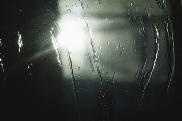 Abstraktes schwarz-weiß Motiv mit Glasscheibe mit Wassermuster vor Himmel mit weißer Sonne und Regen bei Sonnenaufgang am Morgen im Winter
