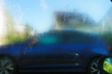 Abstraktes Motiv mit beschlagener Glasscheibe vor parkendem lauen Auto, Wohnhäusern und blauem...