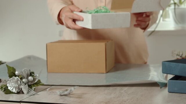Woman placing items into cardboard gift box for Christmas