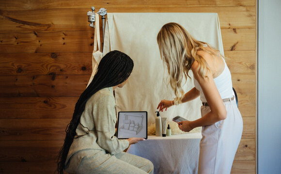 Two creators discussing design ideas with a tablet and cosmetics setup