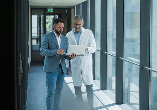Doctor and colleague discussing project with notebook in office corridor