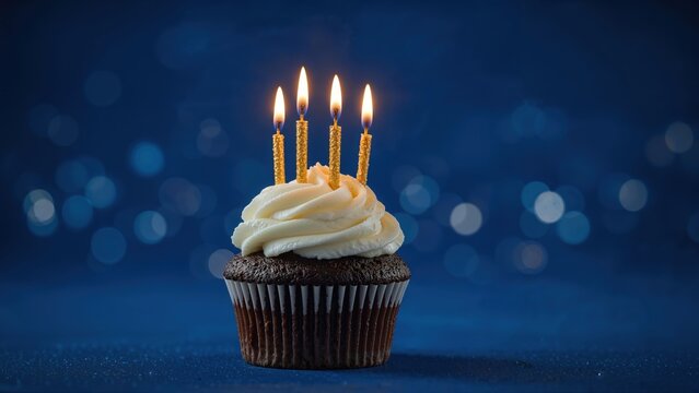 Chocolate cupcake with vanilla frosting and four lit birthday candles on blue bokeh background for celebration and party themes