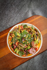 Fresh Mixed Green Salad Bowl with Nuts and Vegetables on Wooden Board Top View