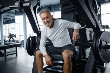 An older gentleman is resting on a training machine in contemporary gym
