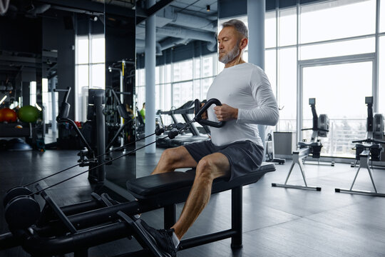 Senior man performs rowing exercise at modern gym