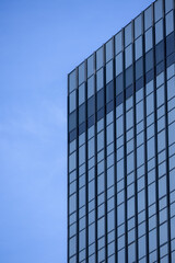 A section of a modern building with many rectangular glass windows reflecting the clear