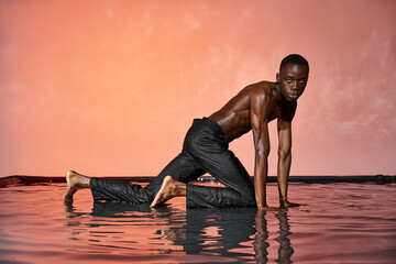 Elegant young man poses in water against a vibrant orange backdrop showcasing fashion and confidence