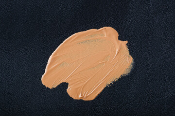 Smudged marks of brown cosmetic substances spread across a textured black leather surface. Daily cosmetic stains foundation on leather upholstery of furniture. top view