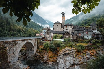 view of Lavertezzo village with a stone bridge over Verzasca river and lush foggy green mountains