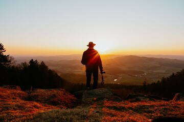 Silhouette of a n man with a camera standing on a hilltop at sunset overlooking a scenic valley