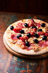 Pizza with ham, salami, tomatoes and mozzarella cheese. Rustic wooden background. Soft focus. Close up.	