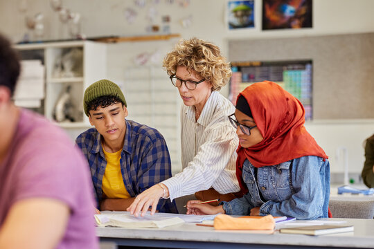 Female teacher assisting teenagers students at high school