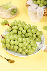 Fresh Green Grapes on Marble Plate with Crystal Glass and Wicker Basket on Yellow Background
