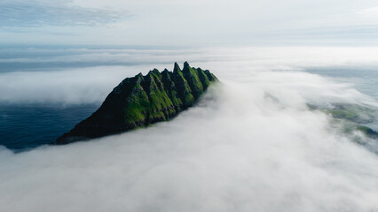 Breathtaking cliffs of the Faroe Islands emerge dramatically from a blanket of clouds, showcasing...