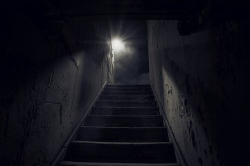 Obraz premium A worn concrete stairway ascends through a narrow, deteriorated corridor. A glowing light at the top breaks the darkness, creating a haunting yet cinematic sense of mystery and anticipation.