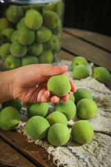 Fresh Green Yunnan Alpine Plums in Hand with Preserved Fruit Jar on Rustic Wood