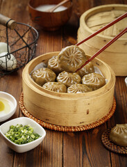 Asian steamed dumplings in bamboo steamer with chopsticks and green onion garnish on wooden table