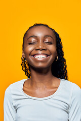 Happy African girl with curly hair smiling brightly against a vibrant yellow background, showcasing...