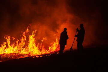Fototapeta premium Silhouettes of two firefighters against night wildfire 