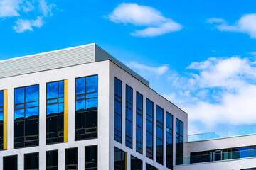 Contemporary office building with reflective blue windows, white fa&ccedil;ade, and minimal yellow accents under bright sky.