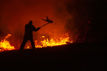 Obraz premium Man fights wildfire at night using improvised tools 
