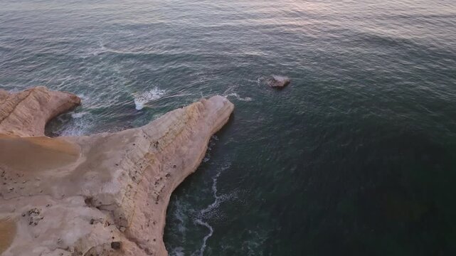 Aerial view of rugged Port Willunga cliffs meeting the tranquil, dark turquoise sea with a small rock island, Port Willunga, South Australia, Australia.