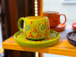 Bright green ceramic cup with floral ornament placed on matching saucer in a shop. Handcrafted artisan design, decorative tradition, and cultural craft symbolism.