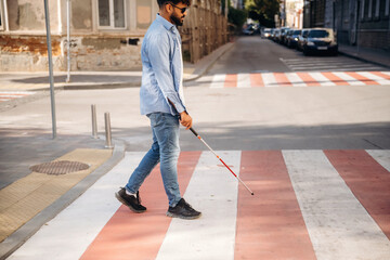 Crossing the road. Blind man with white cane and sunglasses is in the city