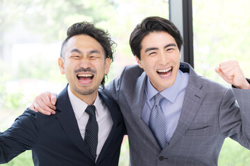 新緑の窓が綺麗なオフィスでビジネスマンのガッツポーズのカメラ目線　達成や成功のイメージ