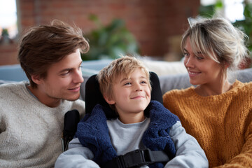 Happy smiling family with son who has disability sitting together on couch. mother and father showing love and care for their child in moment of togetherness at home