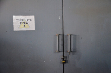 A locked, gray metal door with a sign in Turkish that reads "Tehlikeli Atık Deposu" (Hazardous Waste Depository), symbolizing industrial safety and proper waste management.