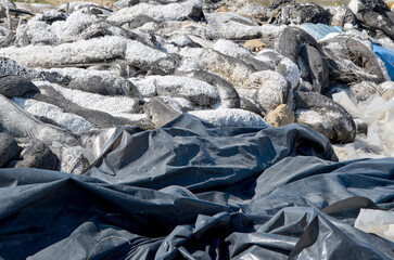 A pile of absorbent material and waste, used to clean up an oil spill at sea, deposited on land, representing a method of environmental cleanup and waste disposal.