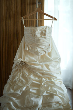 Elegant wedding dress on wooden hanger by window