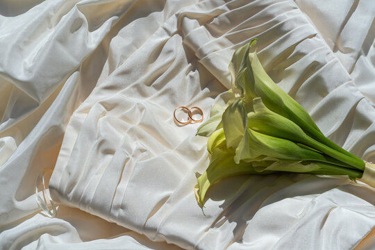 Elegant wedding rings on silky white fabric accompanied by a bouquet