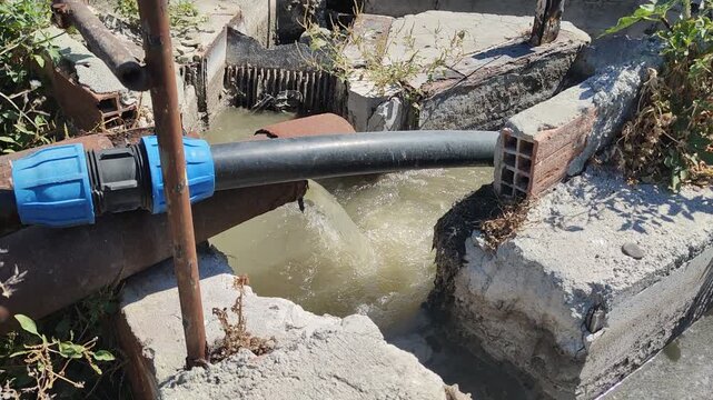  A video of murky, brown water with foam and pollutants discharging from a large concrete outfall into a natural river, highlighting the issue of water pollution.