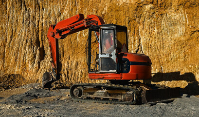 Close up of red excavator at quarry site against rugged rock wall. High quality photo
