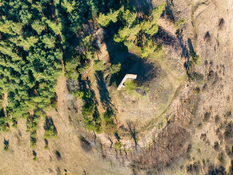 Aerial view of a lone structure atop a small hill surrounded by a ring of dry grass and contrasted by dense green trees, Podz&Atilde;&iexcl;m&Auml;ok, Bansk&Atilde;&iexcl; Bystrica Region, Slovakia.
