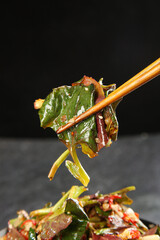 Chopsticks picking up fresh stir-fried vegetables from Asian dish