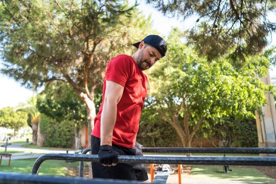 A man in a red shirt exercises on parallel bars at a city park