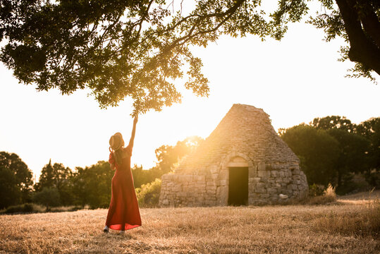 Woman reaching for branch near trulli at sunset in Puglia