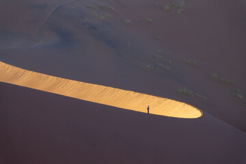 Silhouette of a lone man on Big Daddy sand dune at sunrise in Sossusvlei, Namib Naukluft national park, Namibia abstract landscape, Africa