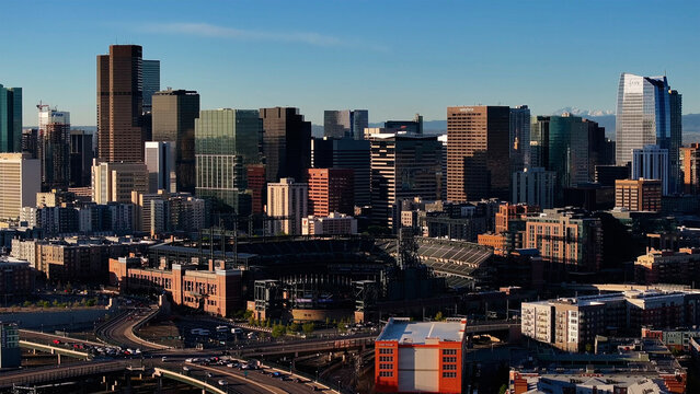 Aerial view of the skyline's towering skyscrapers casting long shadows, blending into the urban landscape, with Coors Field nestled amidst the city's vibrant pulse, Denver, Colorado, United States.