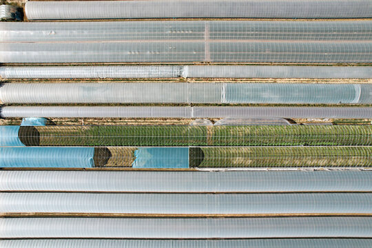 Aerial view of neatly organized greenhouses create a textured tapestry of translucent plastic and verdant growth, showcasing intensive agriculture, Bra, Bra, Italy.